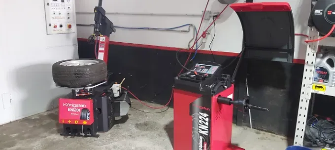 Un neumático en una desmontadora y una equilibradora en un taller. Equipo rojo y negro contra una pared blanca.