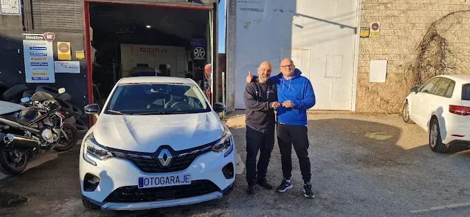Dos hombres sonriendo y dándose la mano delante de un coche Renault blanco en un taller.