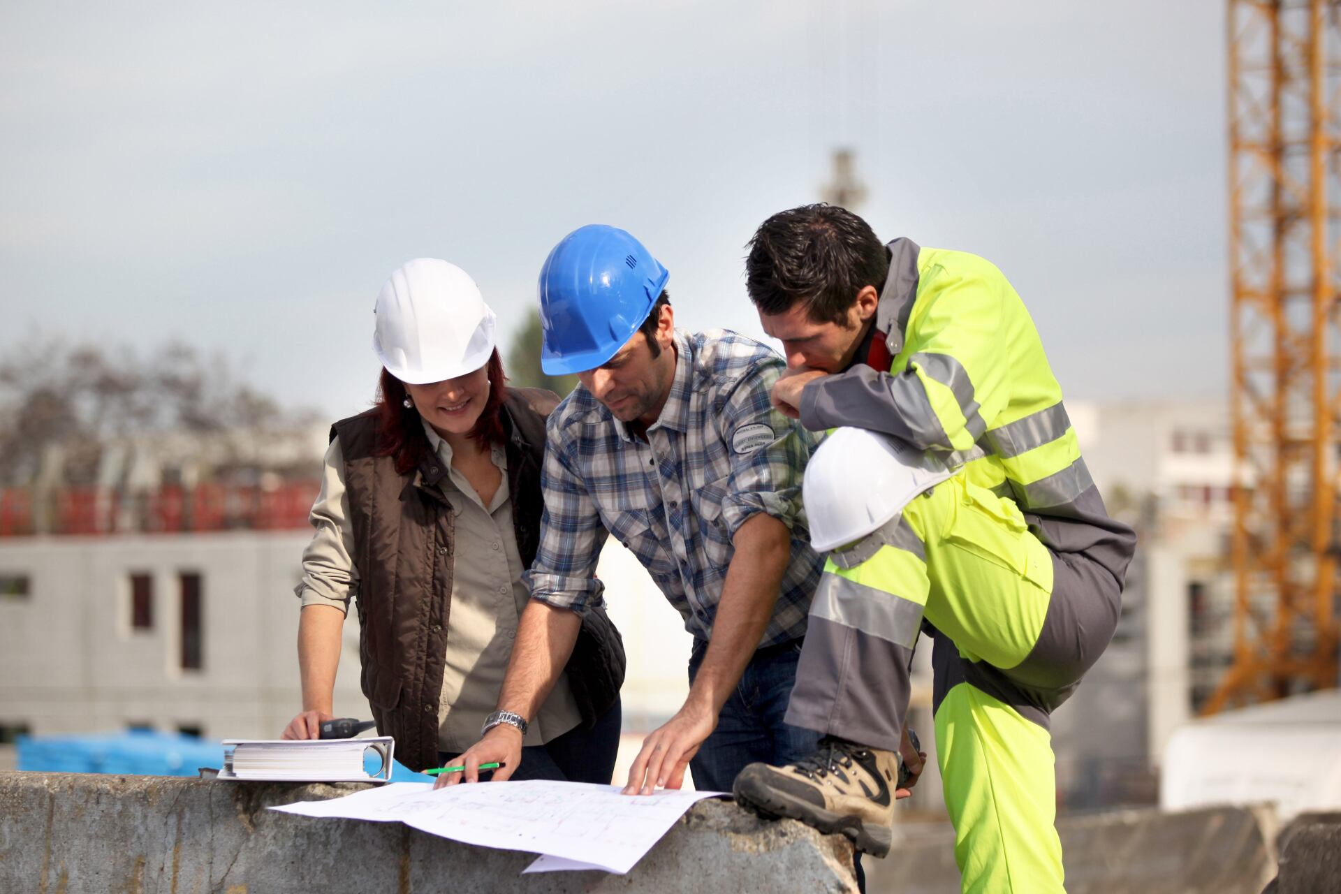 Équipe de trois  techniciens avec casque de chantier regardant un plan