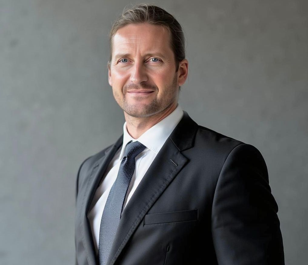 Ein Mann in Anzug und Krawatte lächelt in die Kamera.