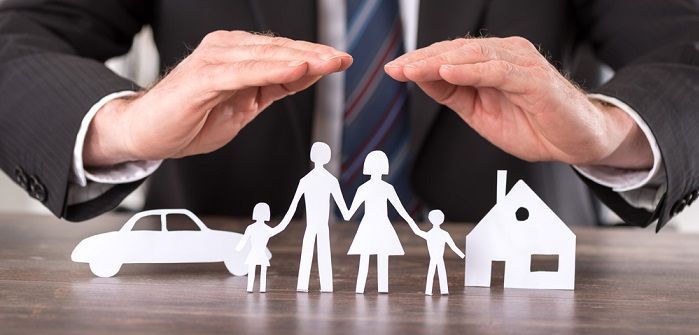 Ein Mann in Anzug und Krawatte bedeckt einen Papierausschnitt einer Familie, eines Autos, eines Hauses und eines Wagens.