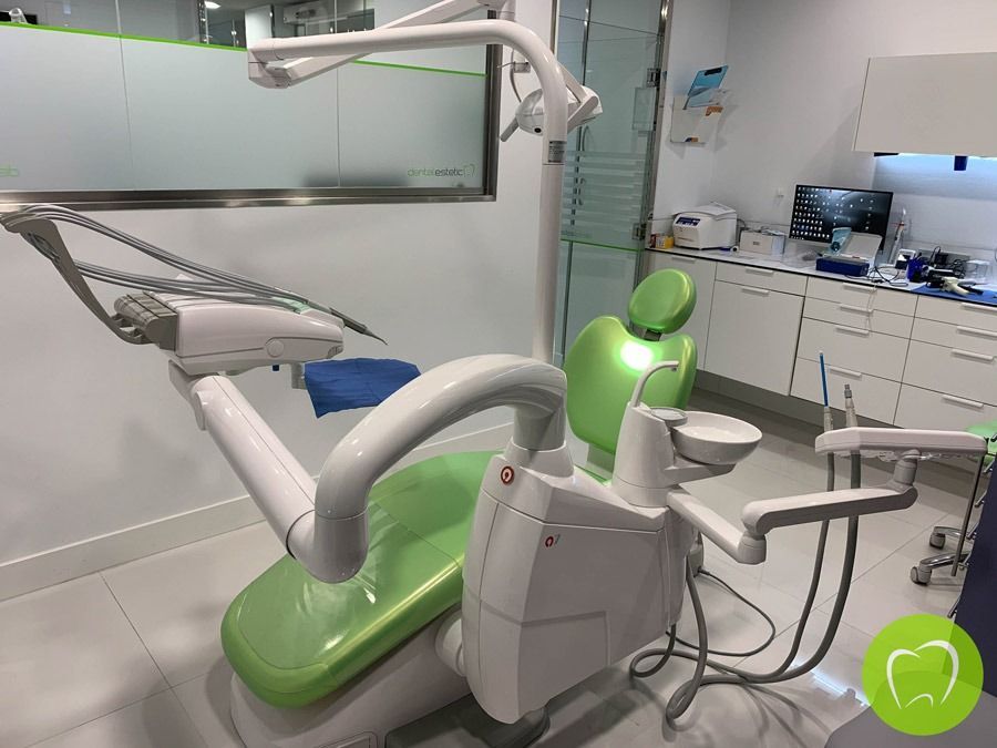 Sillón dental verde en una clínica moderna, con una lámpara de exploración suspendida y brazos para el equipo.