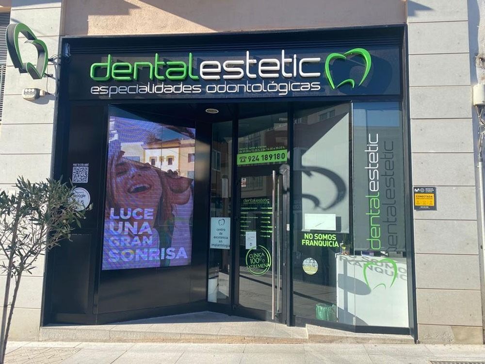 Fachada de Dental Estetic, con un letrero de neón y una entrada de cristal en una calle soleada