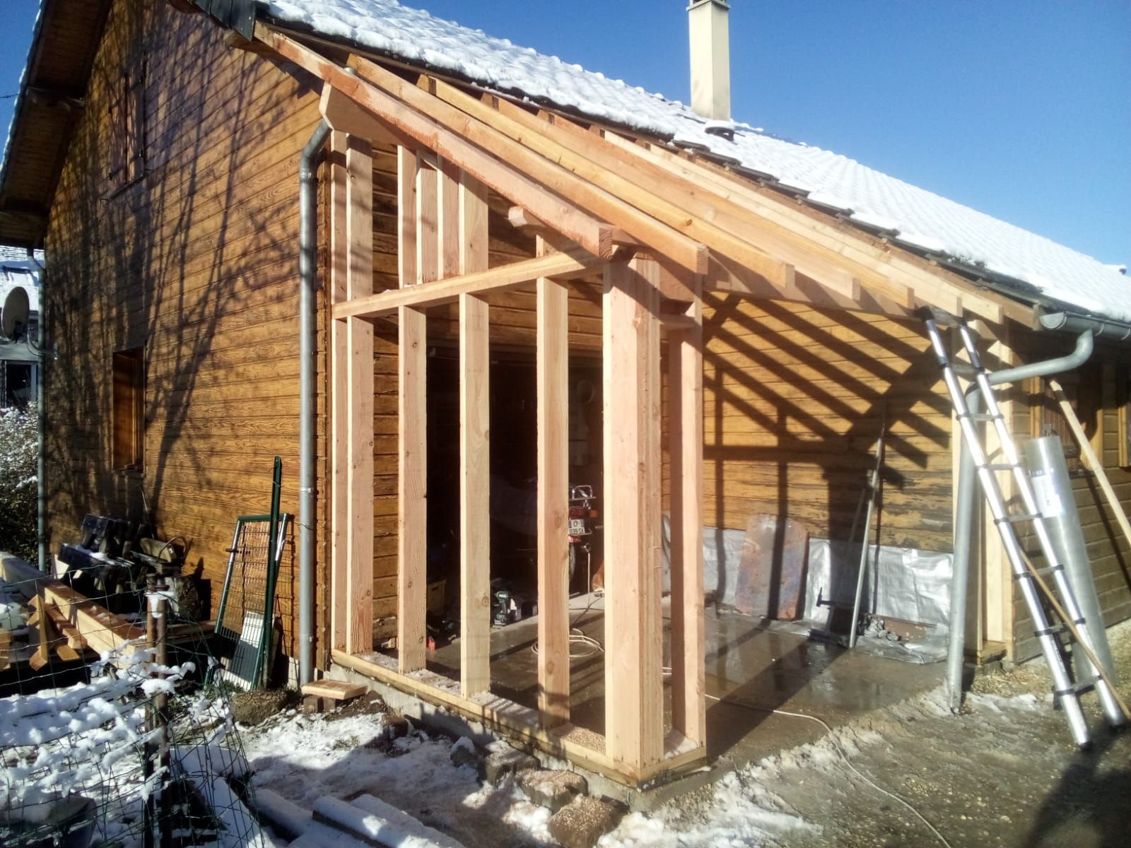 Extension de maison à ossature bois en construction à côté d'un mur de briques, avec un toit en pente.