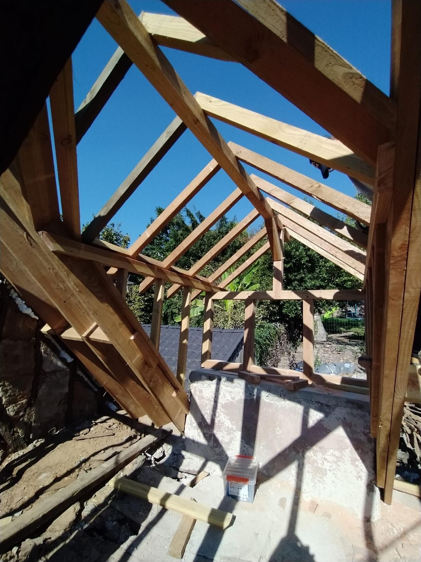 Charpente de toit en bois, avec poutres apparentes et débris, vue de l'intérieur d'une structure partiellement démolie.