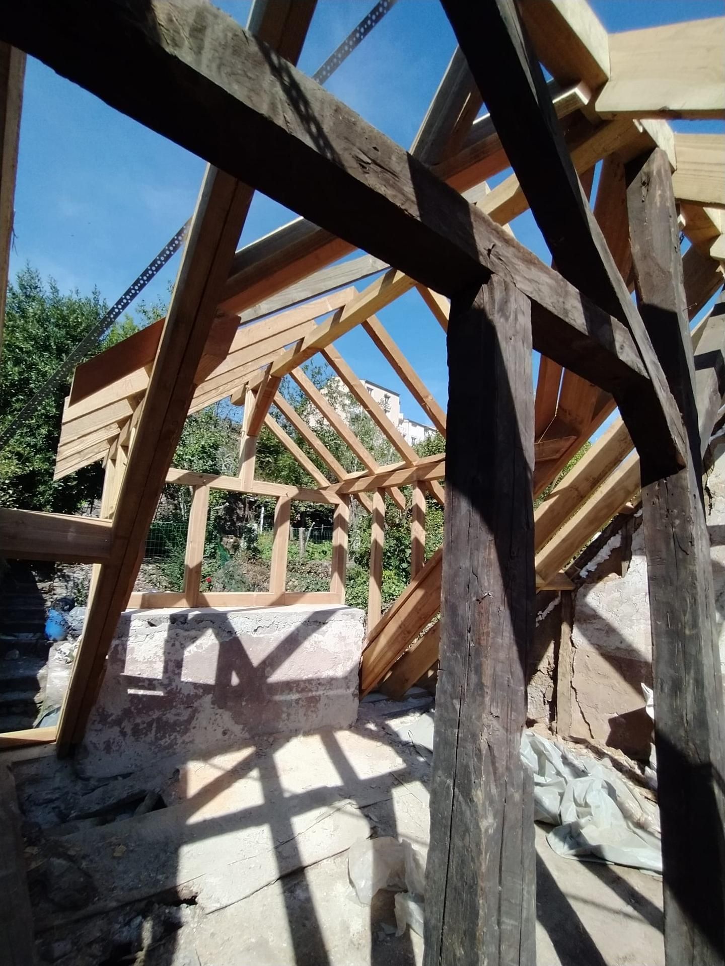 Charpente de toit en bois en construction au-dessus de murs en pierre, laissant apparaître le ciel.