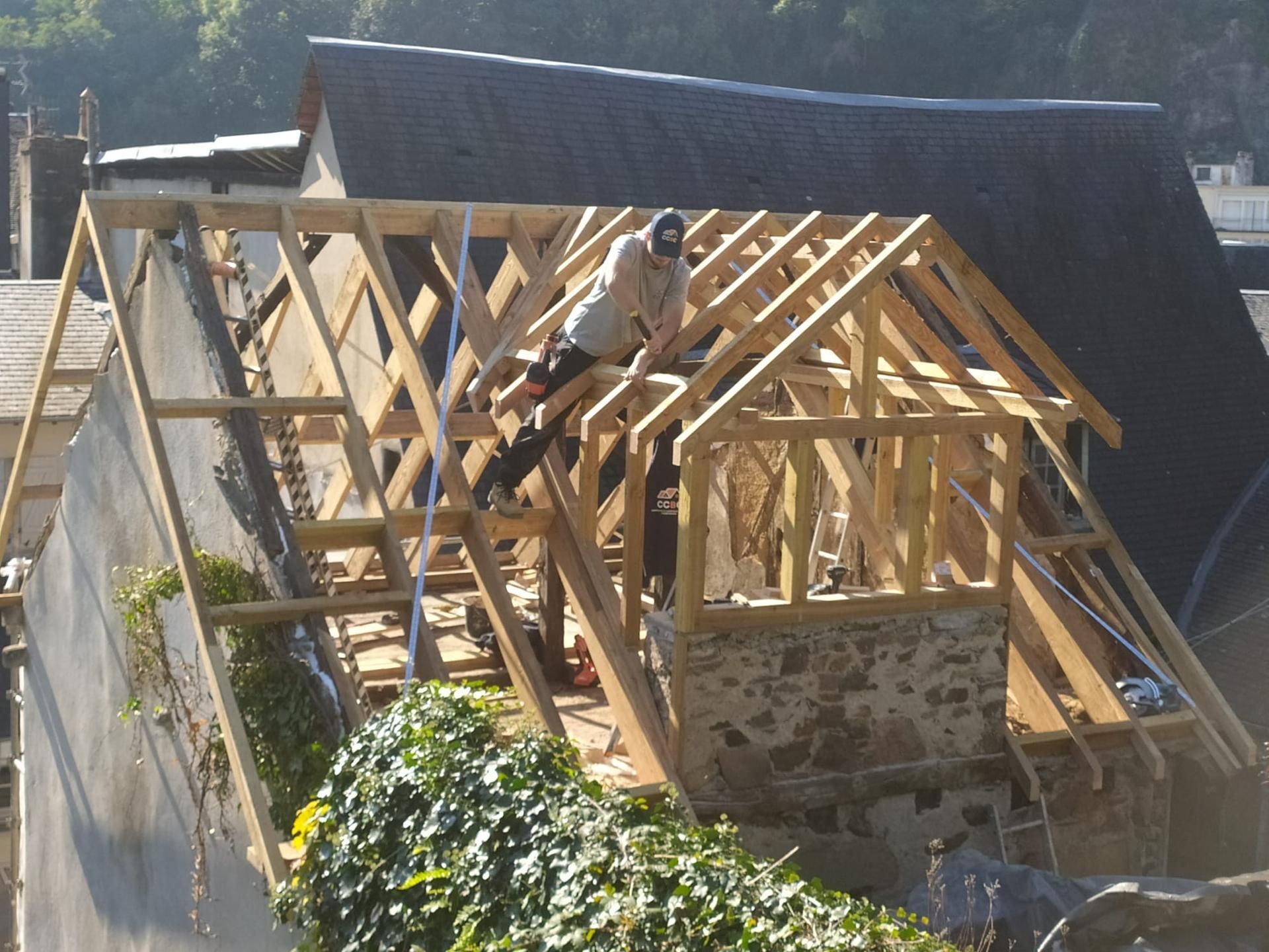 Travaux de construction de toiture en cours sur une maison, avec des chevrons en bois et un ouvrier sur la charpente.