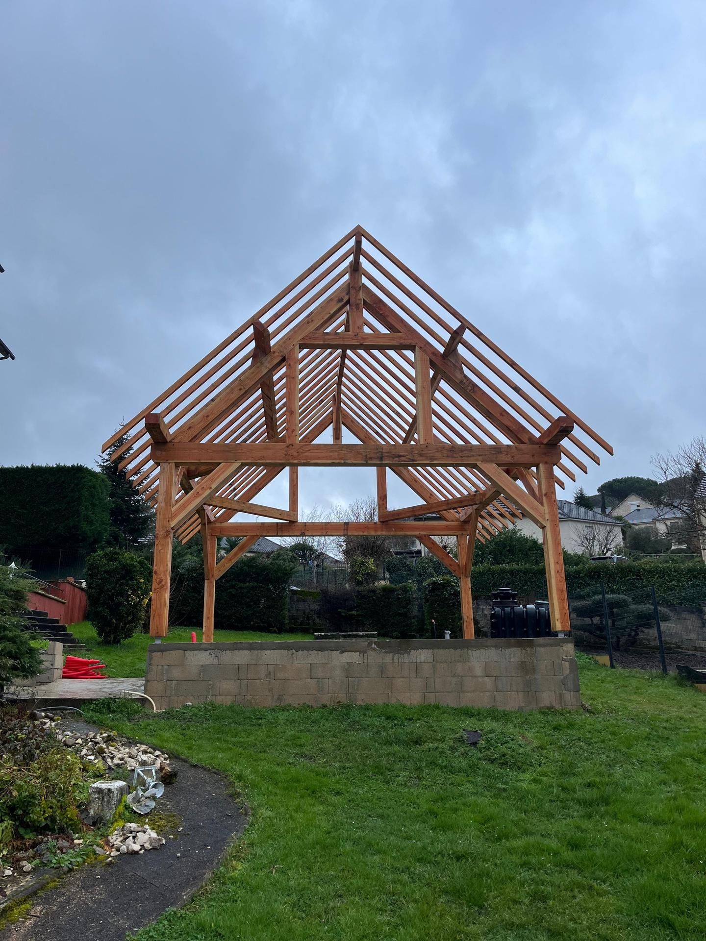 Structure de pavillon en bois sur une base en béton dans un jardin engazonné sous un ciel nuageux