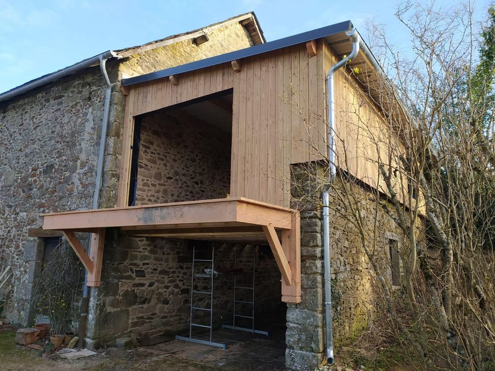 Bâtiment rustique en pierre avec une extension de porche en bois et une charpente de toit apparente.