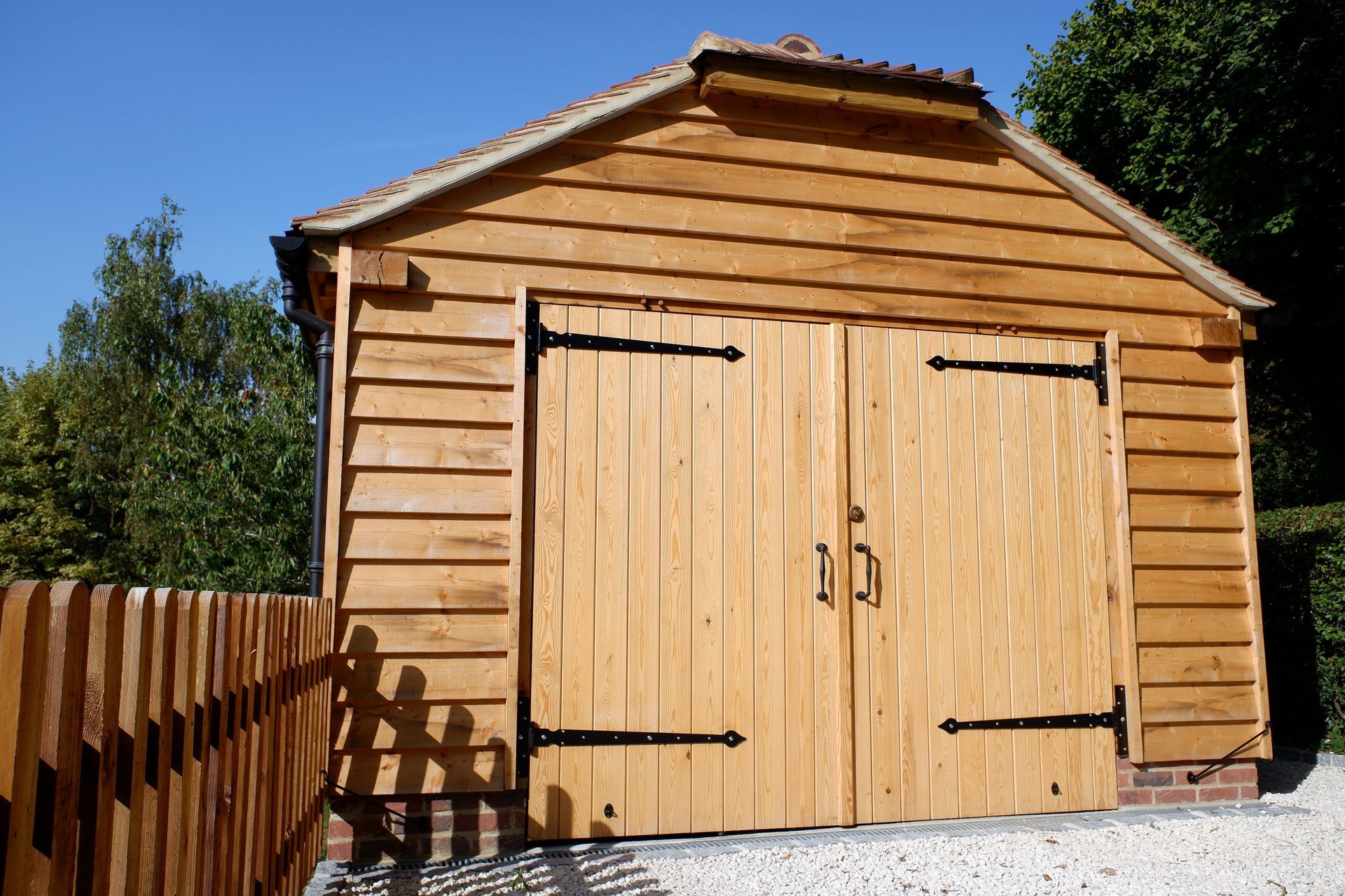 Abri de jardin en bois avec double porte et cour clôturée sous un ciel ensoleillé.