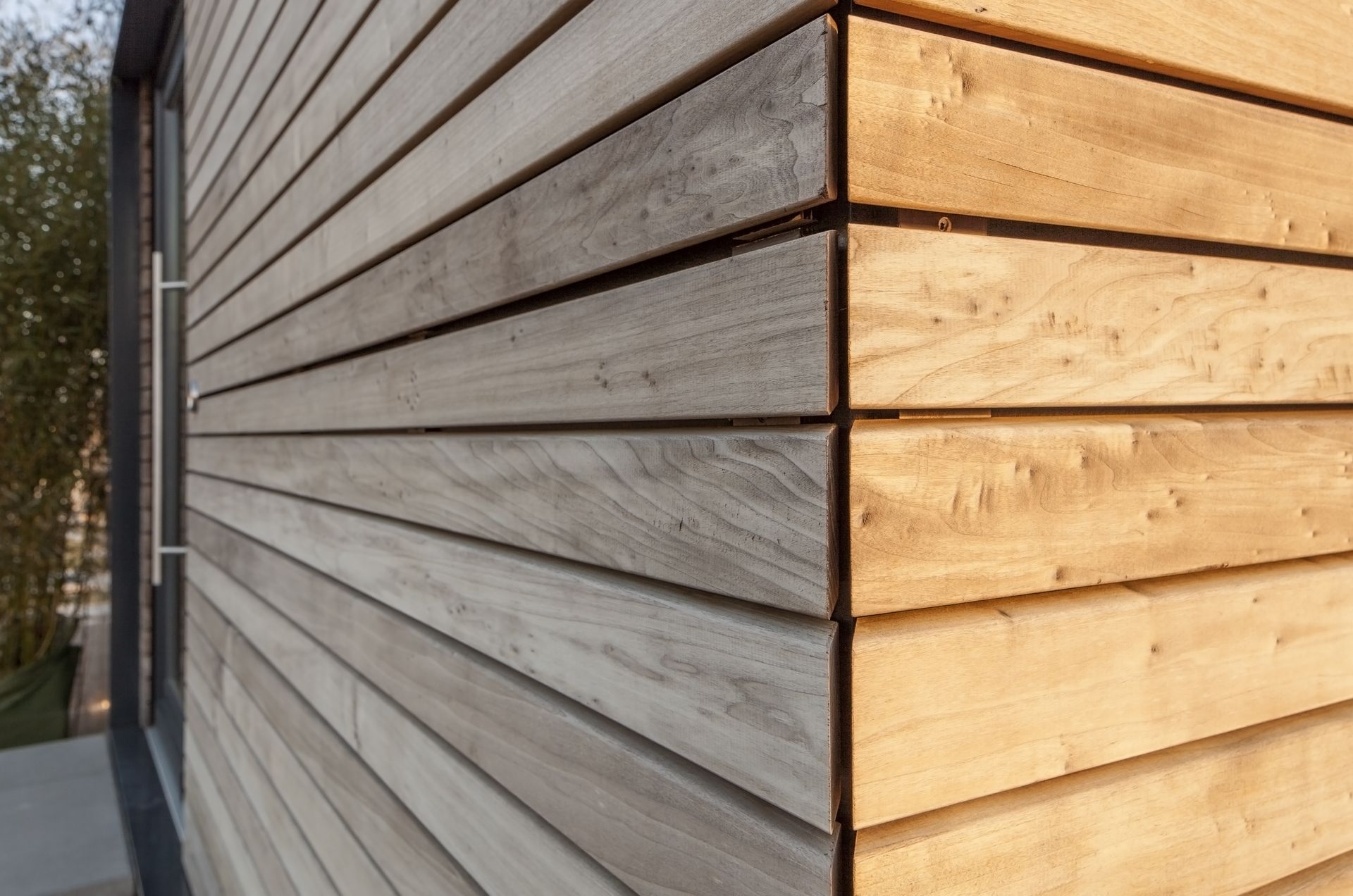 Angle extérieur d'un bâtiment moderne revêtu de bois avec bardage horizontal gris et bois naturel.