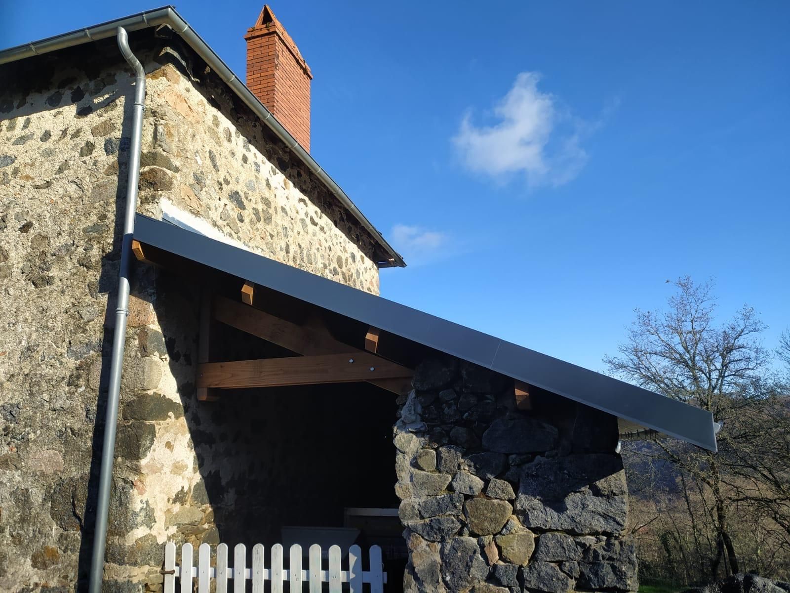 Maison en pierre avec un toit en pente bleu foncé et une cheminée sous un ciel bleu clair.