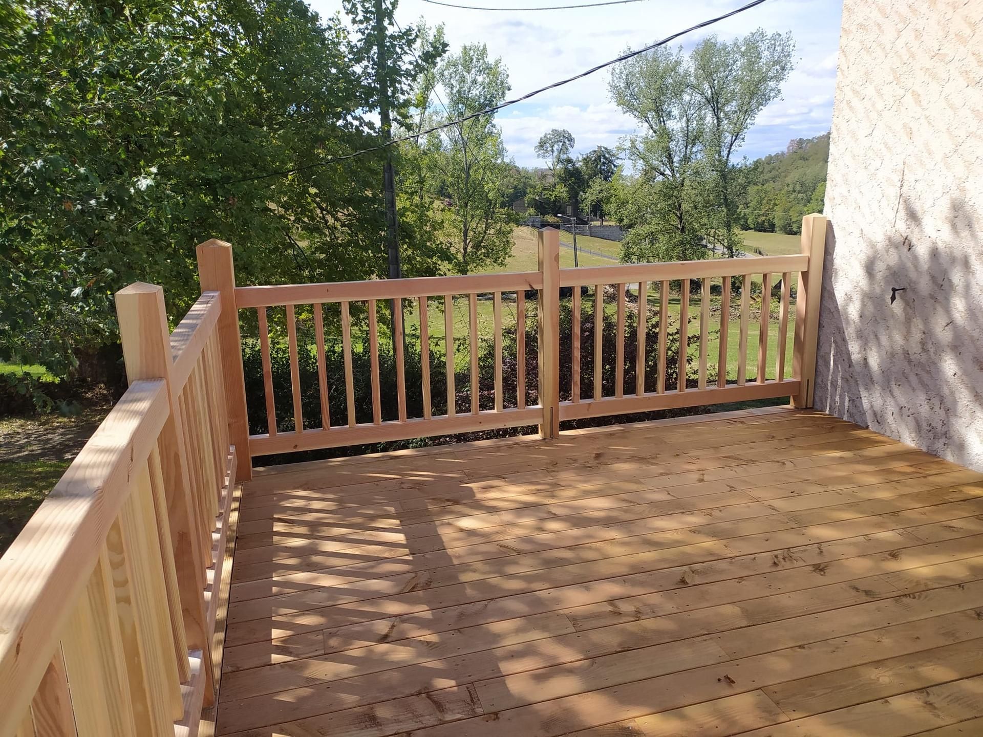 Terrasse en bois avec rambarde donnant sur les arbres et une colline à côté d'une maison blanche.