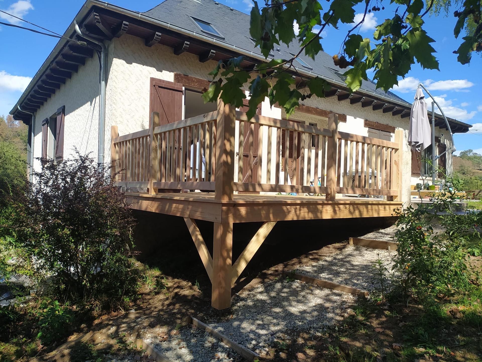 Terrasse en bois d'une maison blanche, vue d'en bas avec des arbres et un ciel bleu au-dessus.