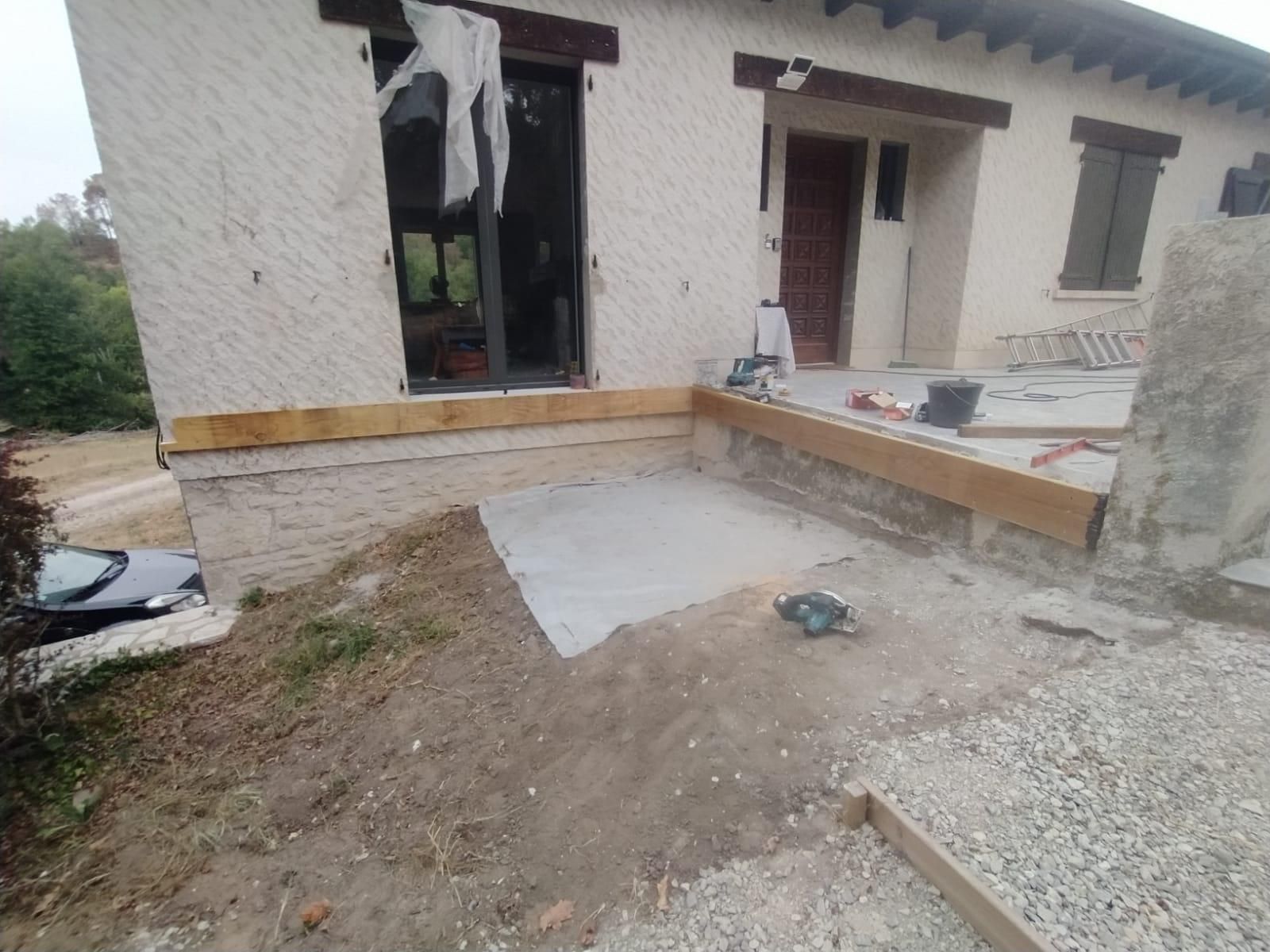 Façade de maison endommagée : fenêtre brisée, débris et terrasse en béton inachevée.