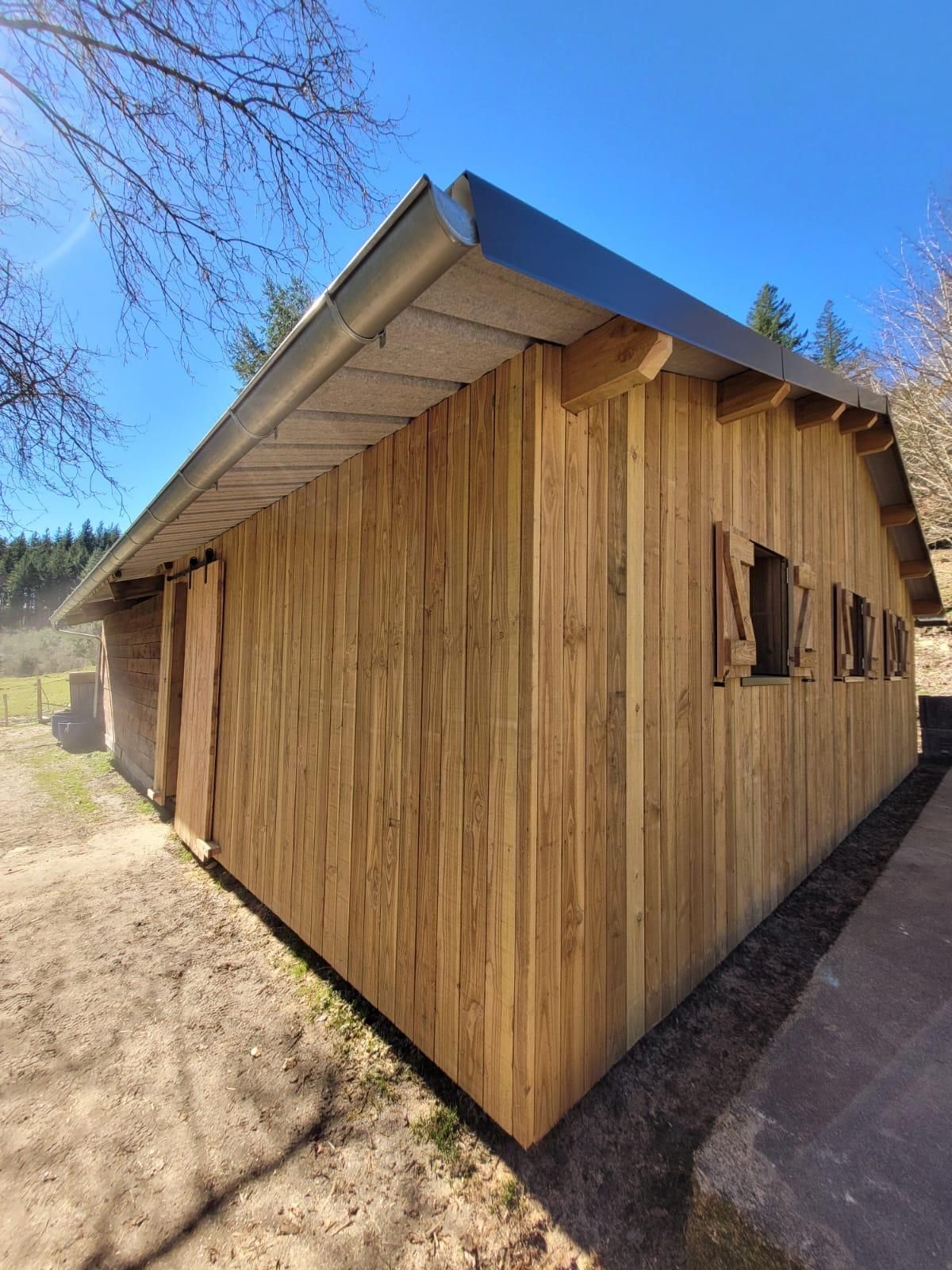 Cabane en bois avec un toit en métal sur un terrain rural ensoleillé.
