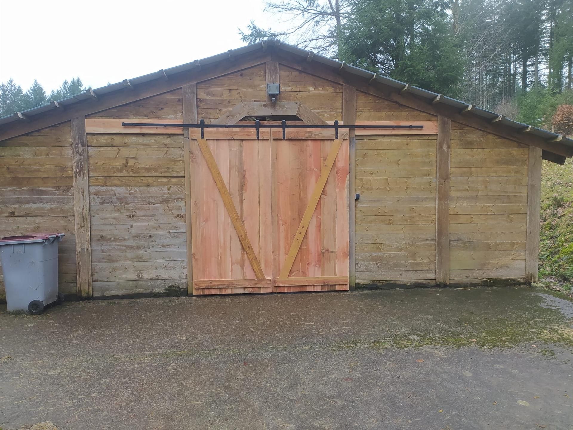 Abri de jardin rustique en bois avec double porte et poubelle à l'extérieur, sur une allée pavée.