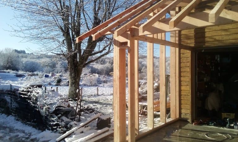 Toit de porche en bois partiellement construit à côté d'une cour arrière enneigée et d'un ruisseau.