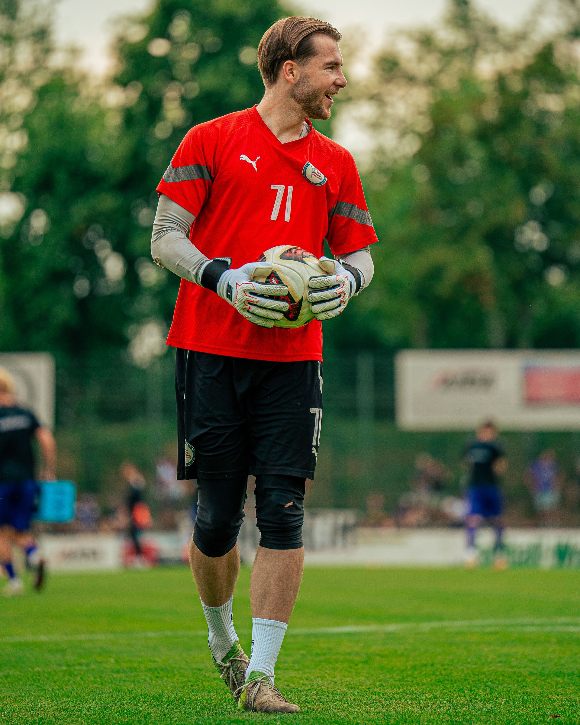Fußballtorwart im roten Trikot hält einen Ball auf einem Rasenfeld