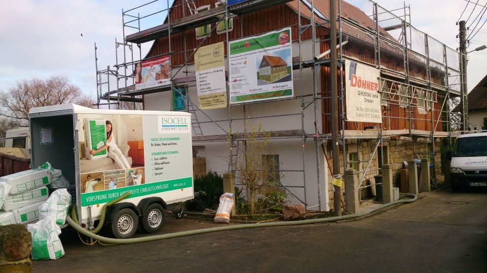 Haus mit Baugerüst und davor geparkter Anhänger mit Dämmmaterial