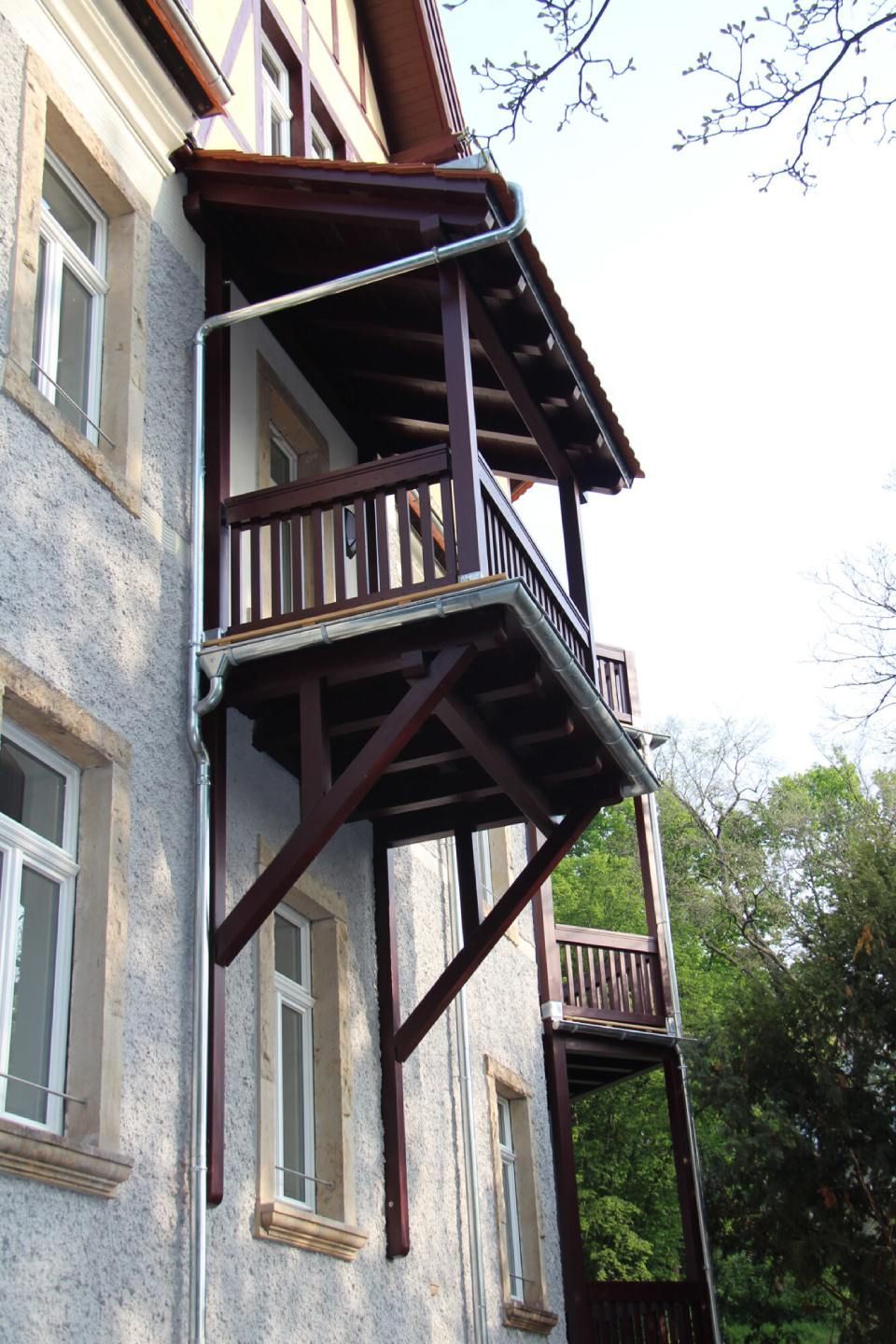 Haus mit Holzterrasse im Erdgeschoß und Holzbalkon im ersten Stock