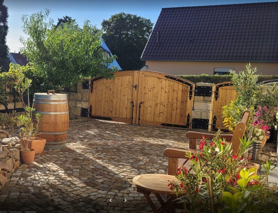 Blick auf Gartentor aus Holz und Steinboden, Gartenstuhl und Pflanzen, Holzfass
