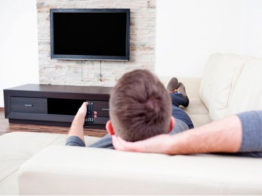 Un hombre está acostado en un sofá mirando la televisión.