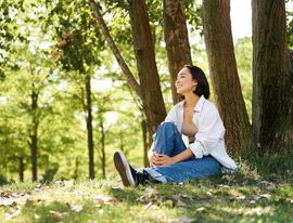 Una persona sentada en el césped de un parque soleado, leyendo un libro bajo los árboles.