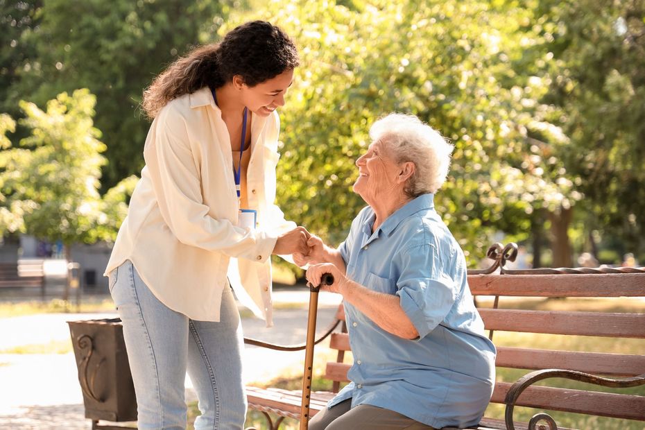 Une jeune femme debout et une femme âgée assise sur un banc.