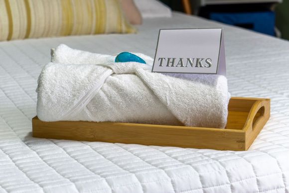 Towel folded in a wooden tray on a bed with a &ldquo;THANKS&rdquo; card and teal soap bar