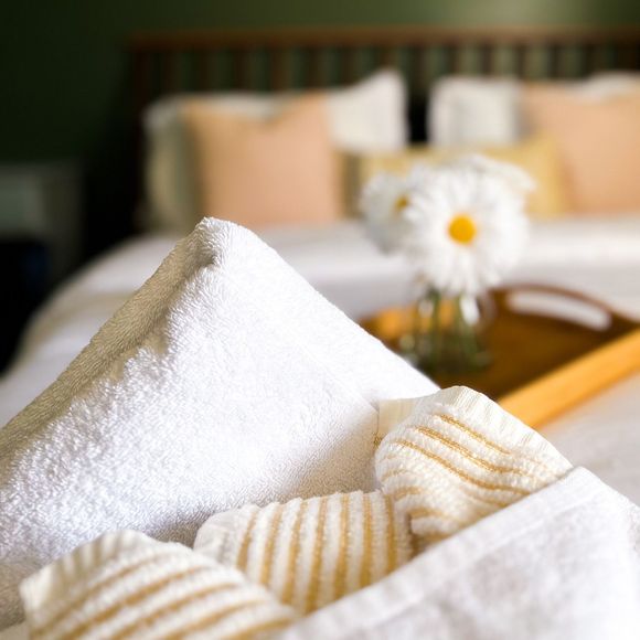 White towels folded on a bed in a hotel room, with a flower vase on the bedside table.