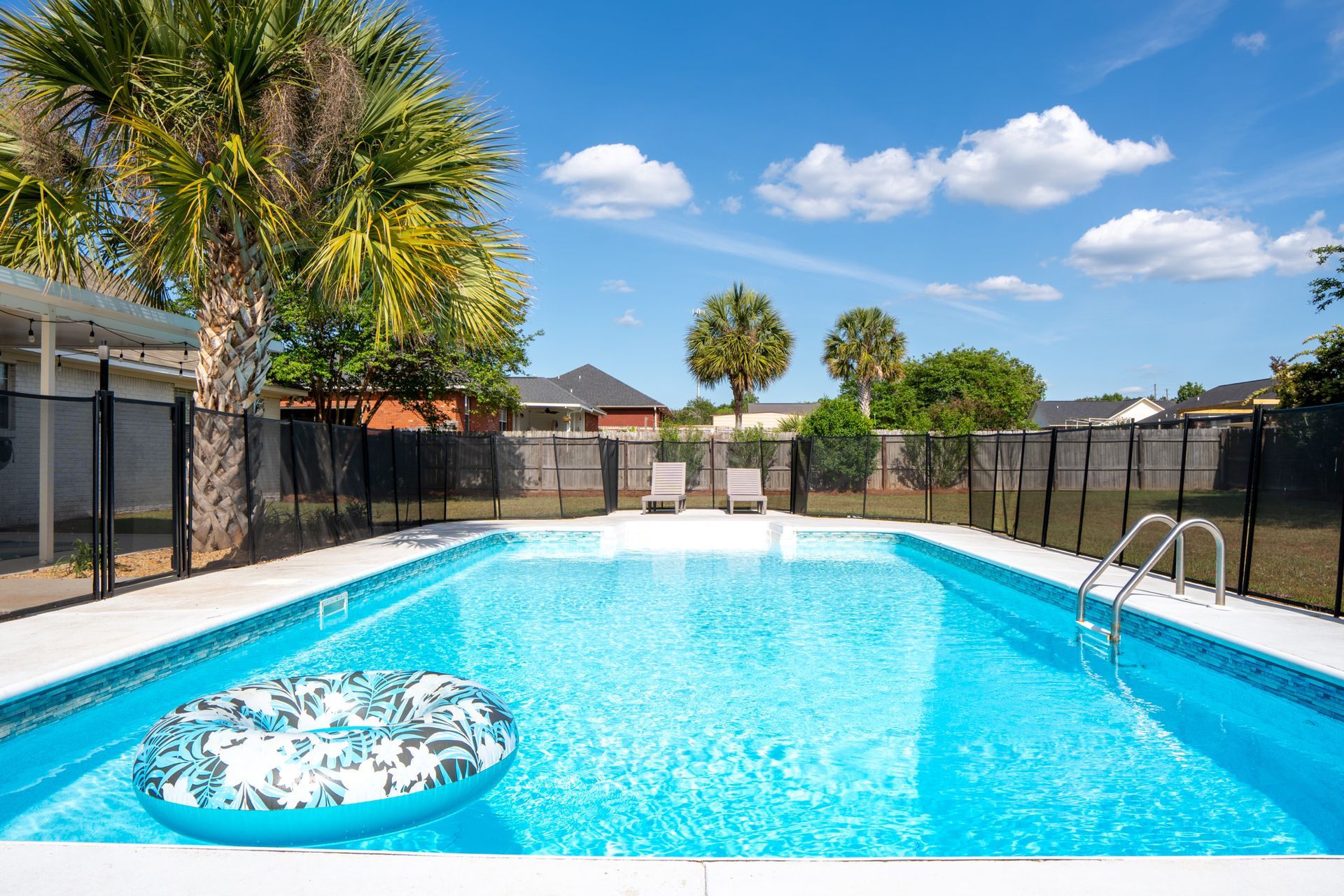 Outdoor swimming pool with bright blue water, palm trees, and lounge chairs under a sunny sky