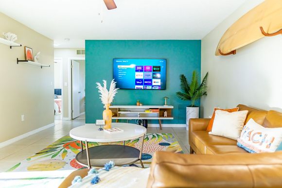 Bright living room with teal TV wall, tan sofa, round coffee table, and colorful rug