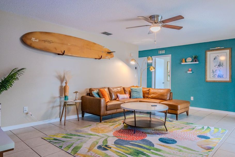 Bright living room with teal accent wall, tan sectional, surfboard decor, and colorful rug