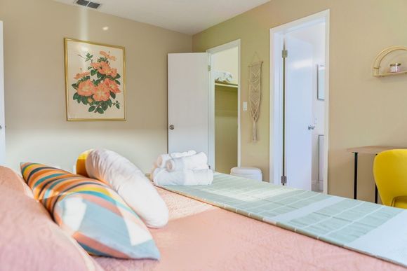 Bright bedroom with pastel bedding, floral wall art, and a mirrored closet door