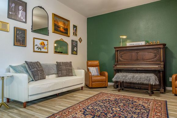 Cozy living room with white sofa, gallery wall art, green accent wall, upright piano, and patterned rug