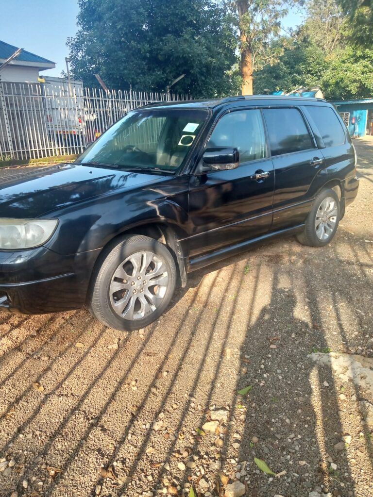 A black subaru forester is parked in a gravel lot.