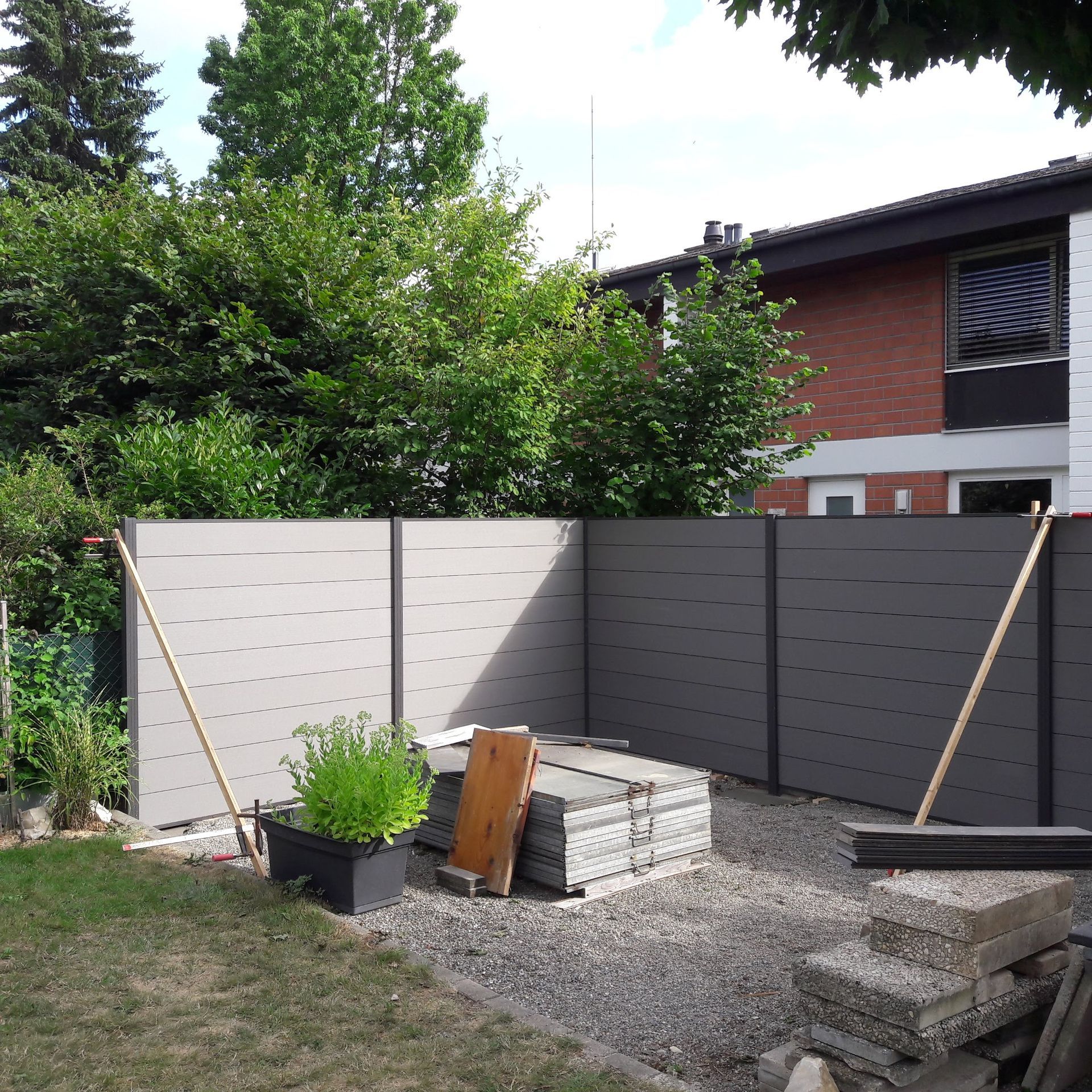 Die Installation eines grauen Sichtschutzzauns in einem Wohngarten, in der Nähe von Baumaterialien und einer Pflanze.
