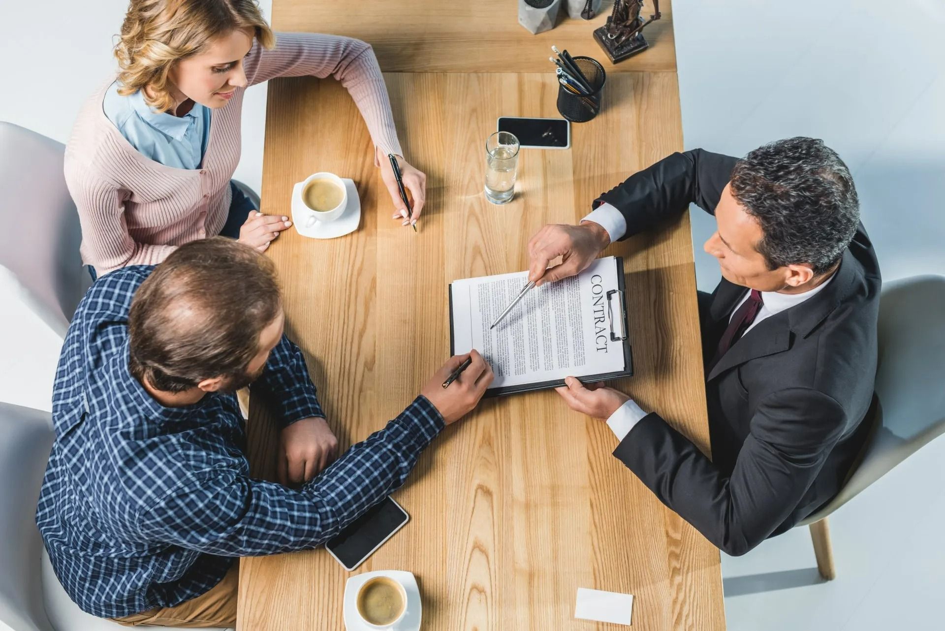 Un couple et leur conseiller sont assis à une table et examinent des documents. Le conseiller désigne un document. Des tasses de café sont posées sur la table.