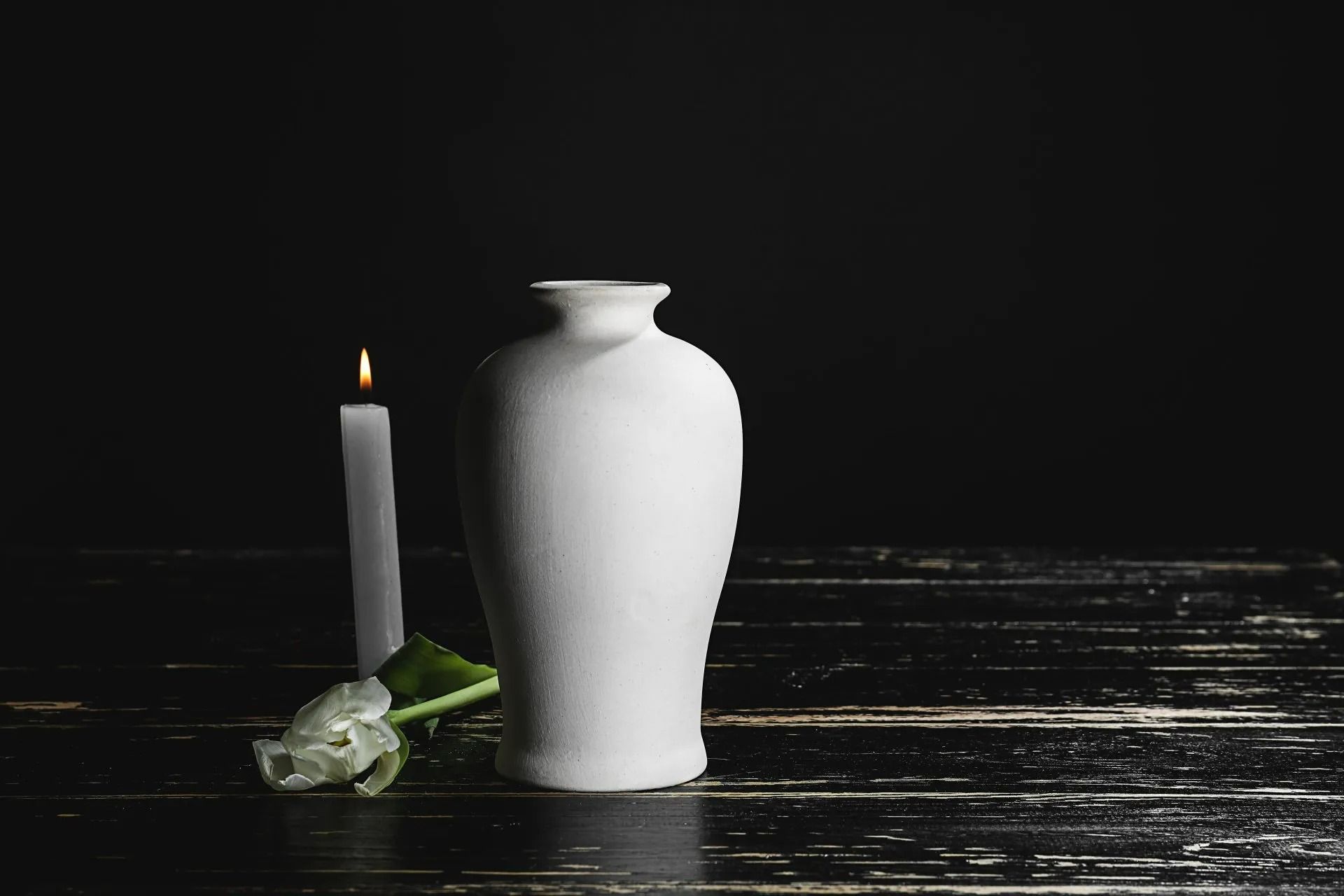 Vase blanc et bougie allumée sur une surface en bois foncé.