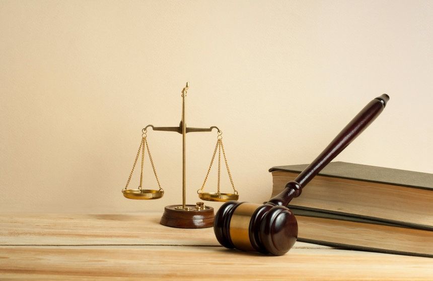 Un mazo de juez de madera, una balanza de justicia y libros sobre una mesa de madera.