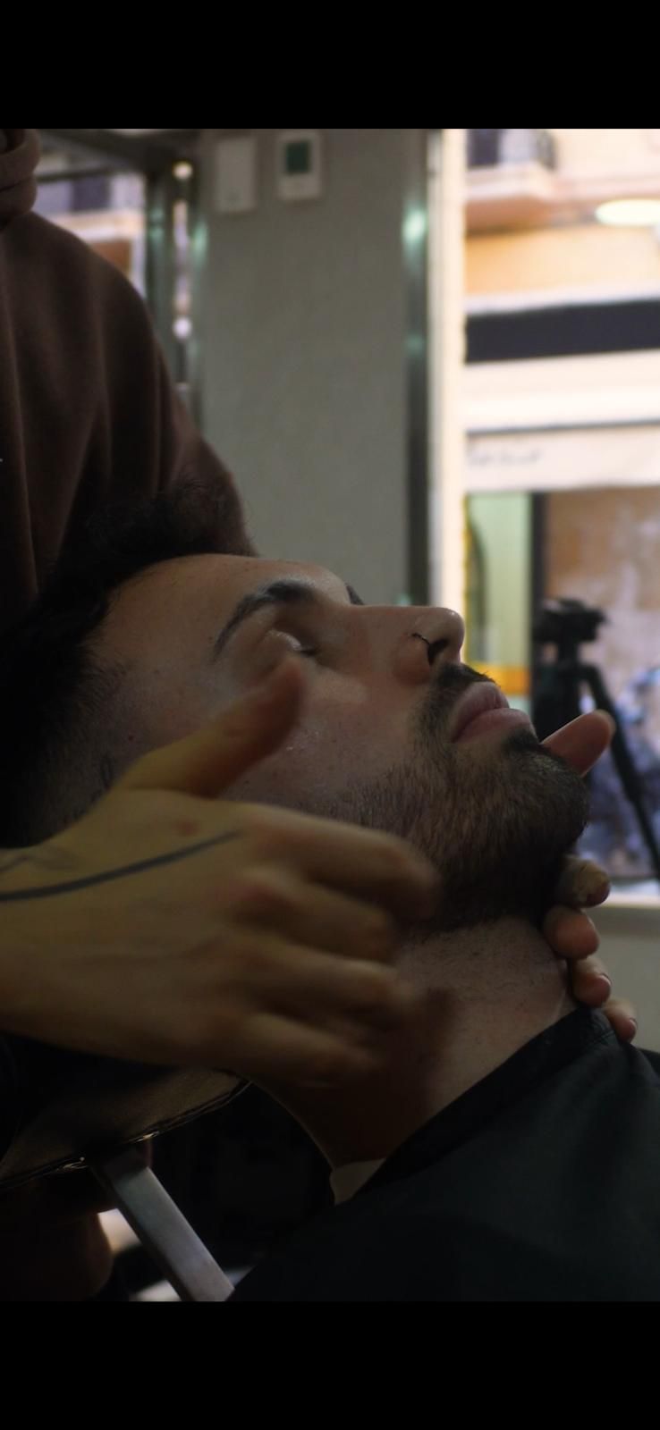 Hombre con el pelo descolorido y teñido de plata. Está en una barbería, con capa.