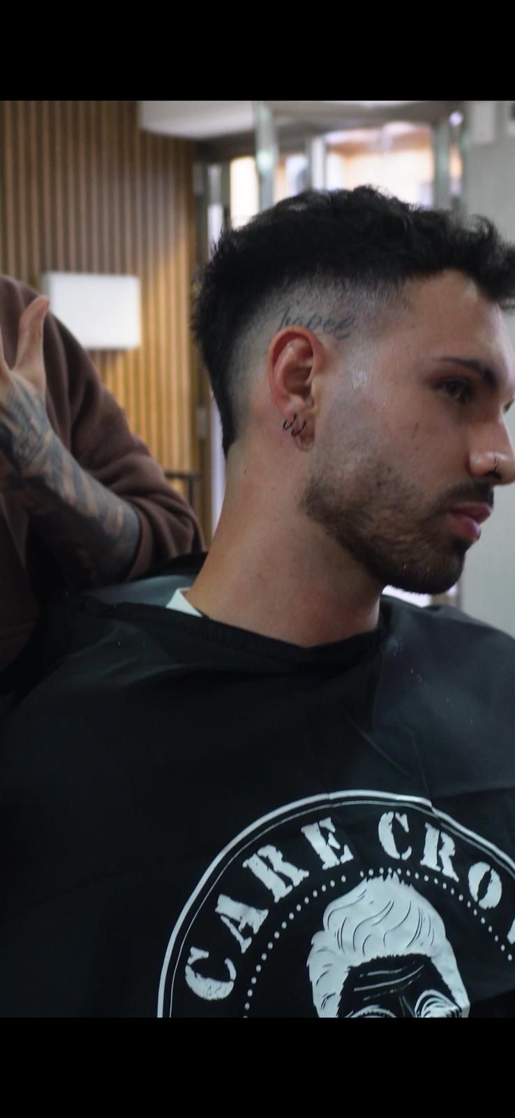 Hombre con cabello corto, corte de pelo desvanecido, mirando hacia abajo en un salón.