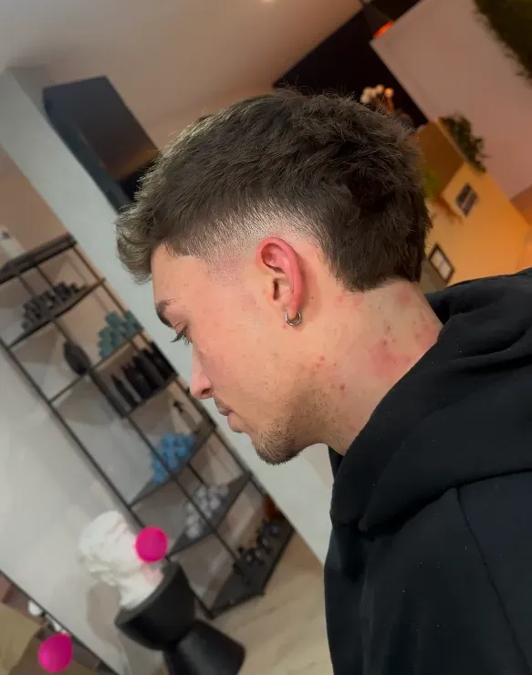 Hombre con cabello corto, corte de pelo desvanecido, mirando hacia abajo en un salón.