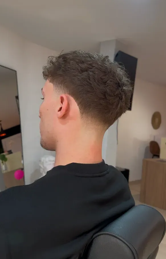 Hombre con el pelo descolorido y teñido de plata. Está en una barbería, con capa.