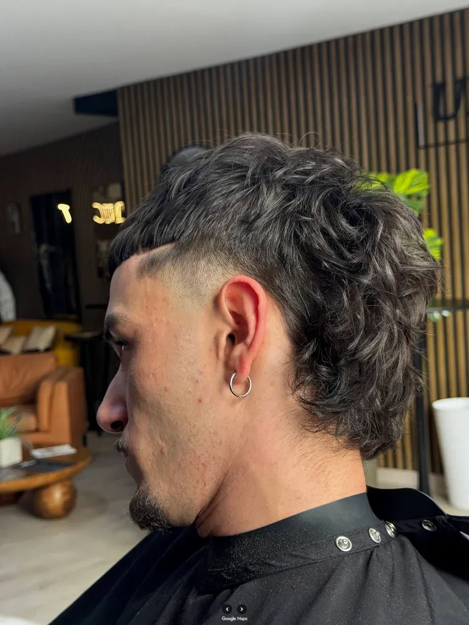 Hombre con un corte de pelo mullet rizado, con un desvanecimiento bajo en los lados, en un salón de belleza.