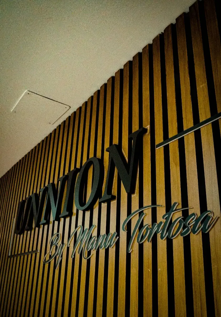 Acogedora sala de espera con sofá amarillo, sillón marrón, pared revestida de madera, espejo, mesa pequeña y arte enmarcado.