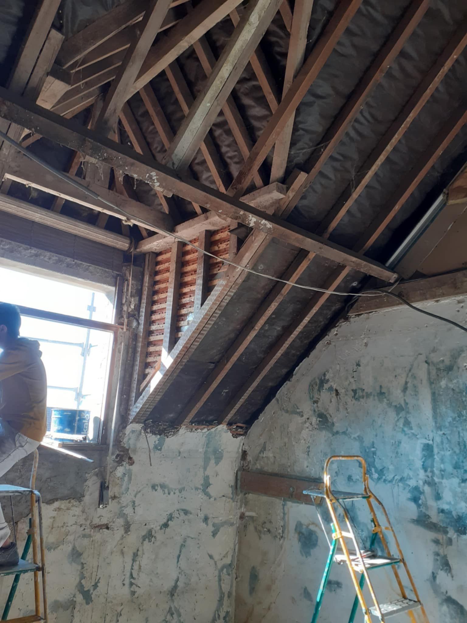 Vue intérieure d'une pièce en construction avec charpente apparente et une fenêtre.