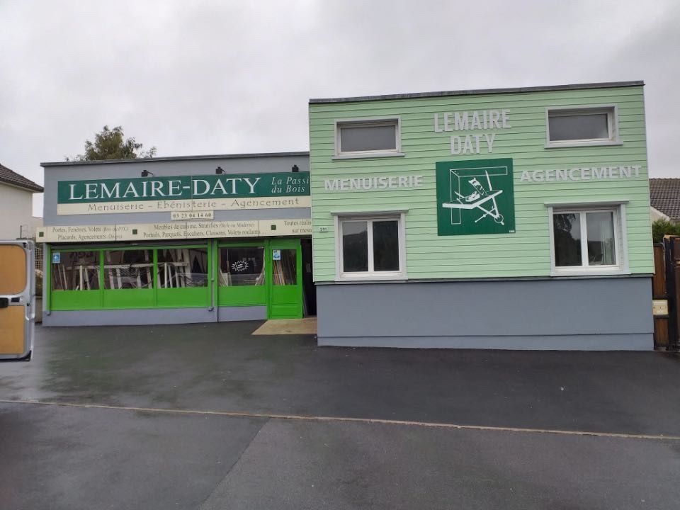 Façade du bâtiment avec l'enseigne « LEMAIRE-DATY » en vert et blanc, fond gris et béton.