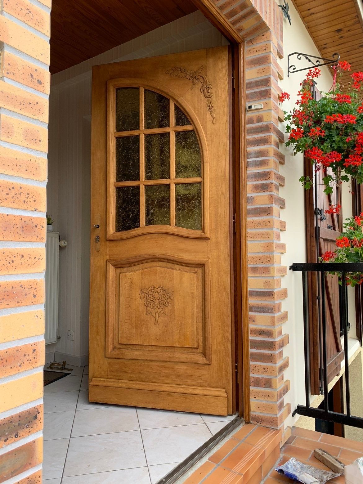 Porte en bois ouverte avec vitre dans une façade en briques et en stuc.
